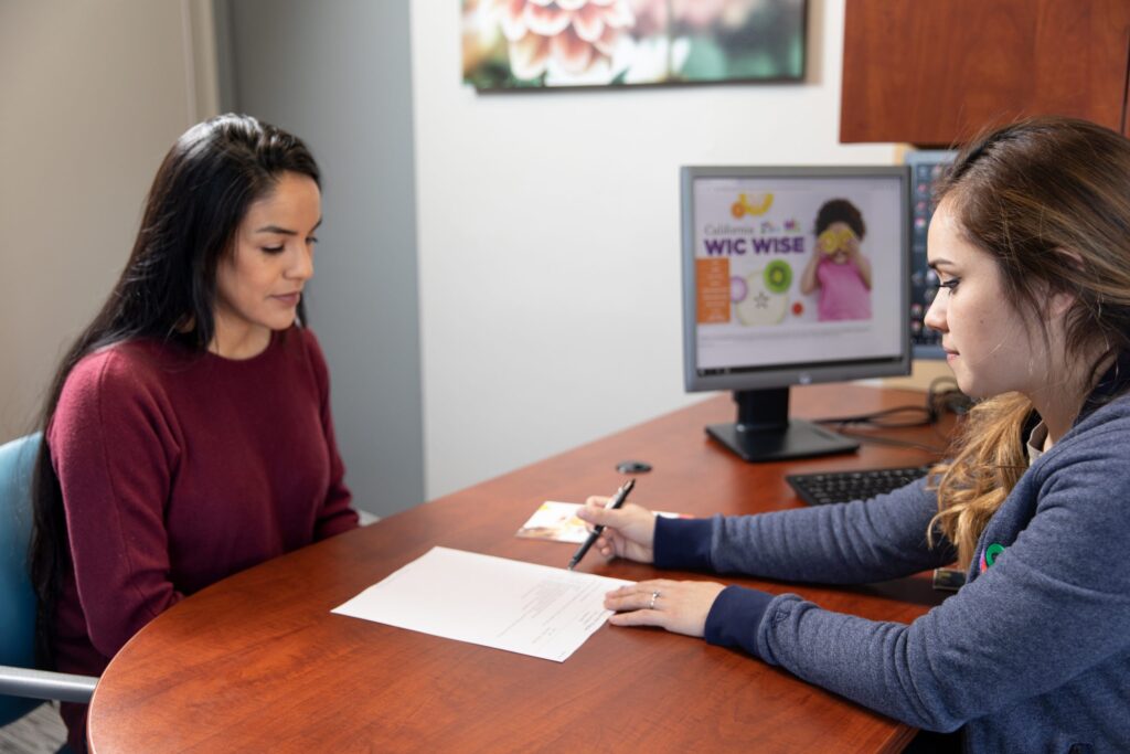 A WIC counselor is reviewing information on a paper with a WIC participant across the desk.